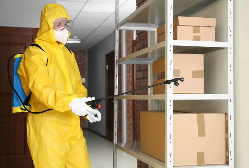 Person in hazmat suit spraying storage shelves.